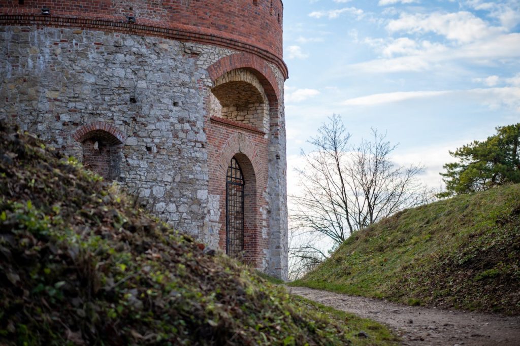 Old stone castle tower with arch and door, surrounded by nature on a bright day.